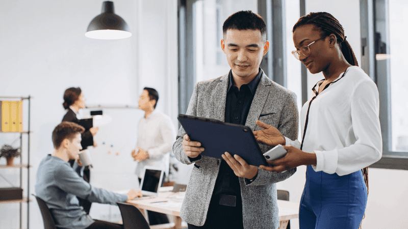 African businesswoman and Asian businessman using a tablet with interracial group of business men & women team